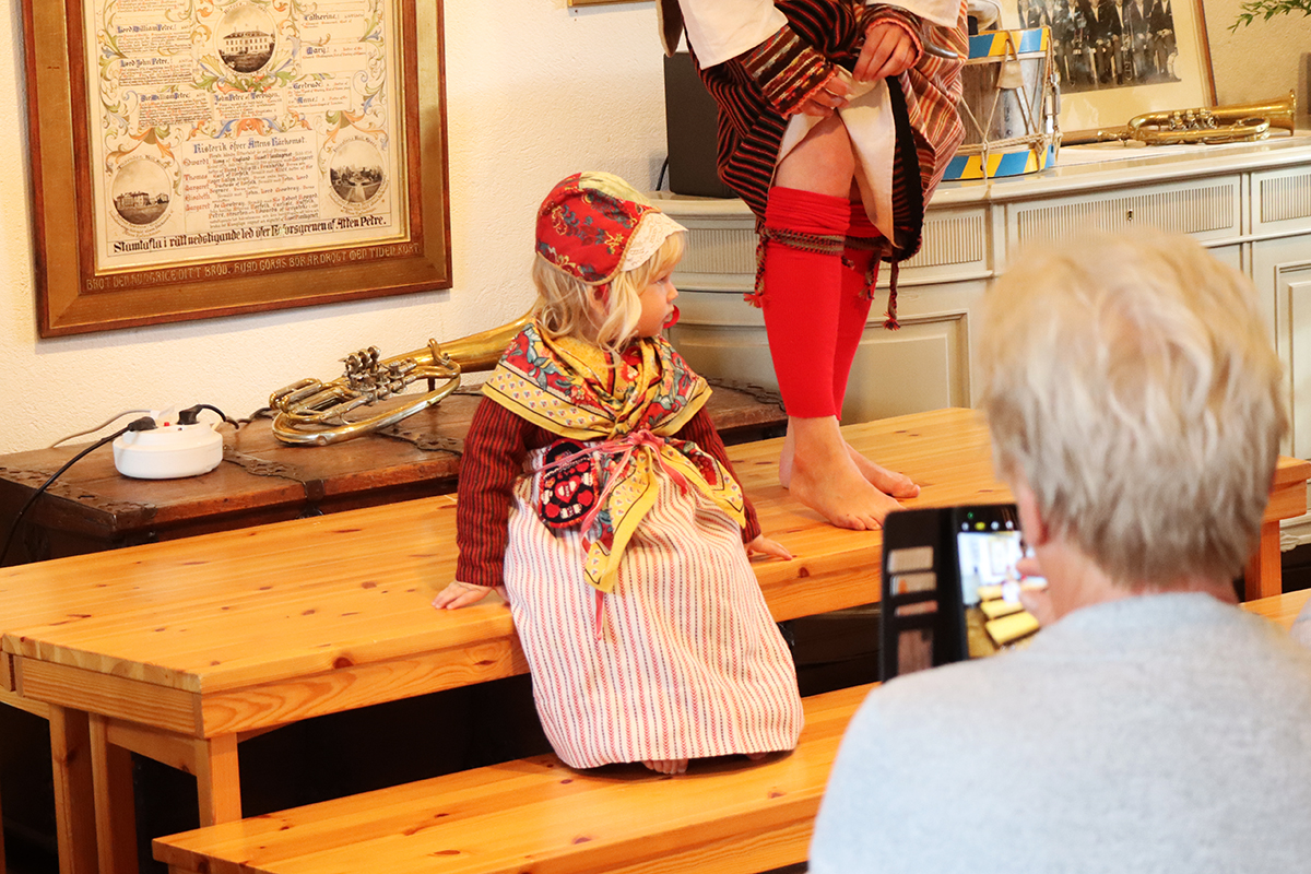 Liten tös i kolt i randig ylle, sk pärk. Hemvävt förkläde, kattun i mössa och halsduk. Liten kjolsäck med applikationer. Modell Maj som nästan stal hela showen med sitt naturliga sätt.