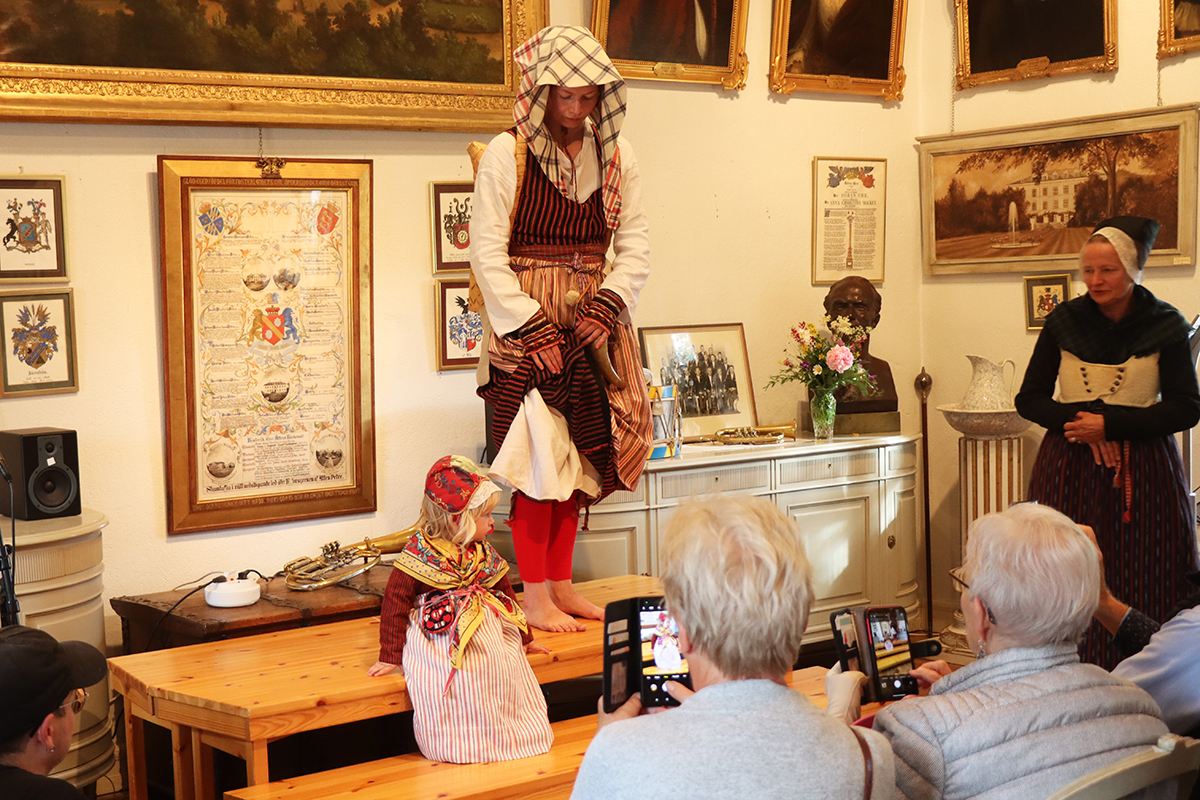 Vallpiga från fäboden med kont på ryggen. Hemvävda material i livkjol i ylle och randigt linneförkläde. Hylka i kattun under rutigt huvudkläde. Enkel vit särk under livkjolen. Strumpskaft i rött på benen. Modell Kristin Sundberg.