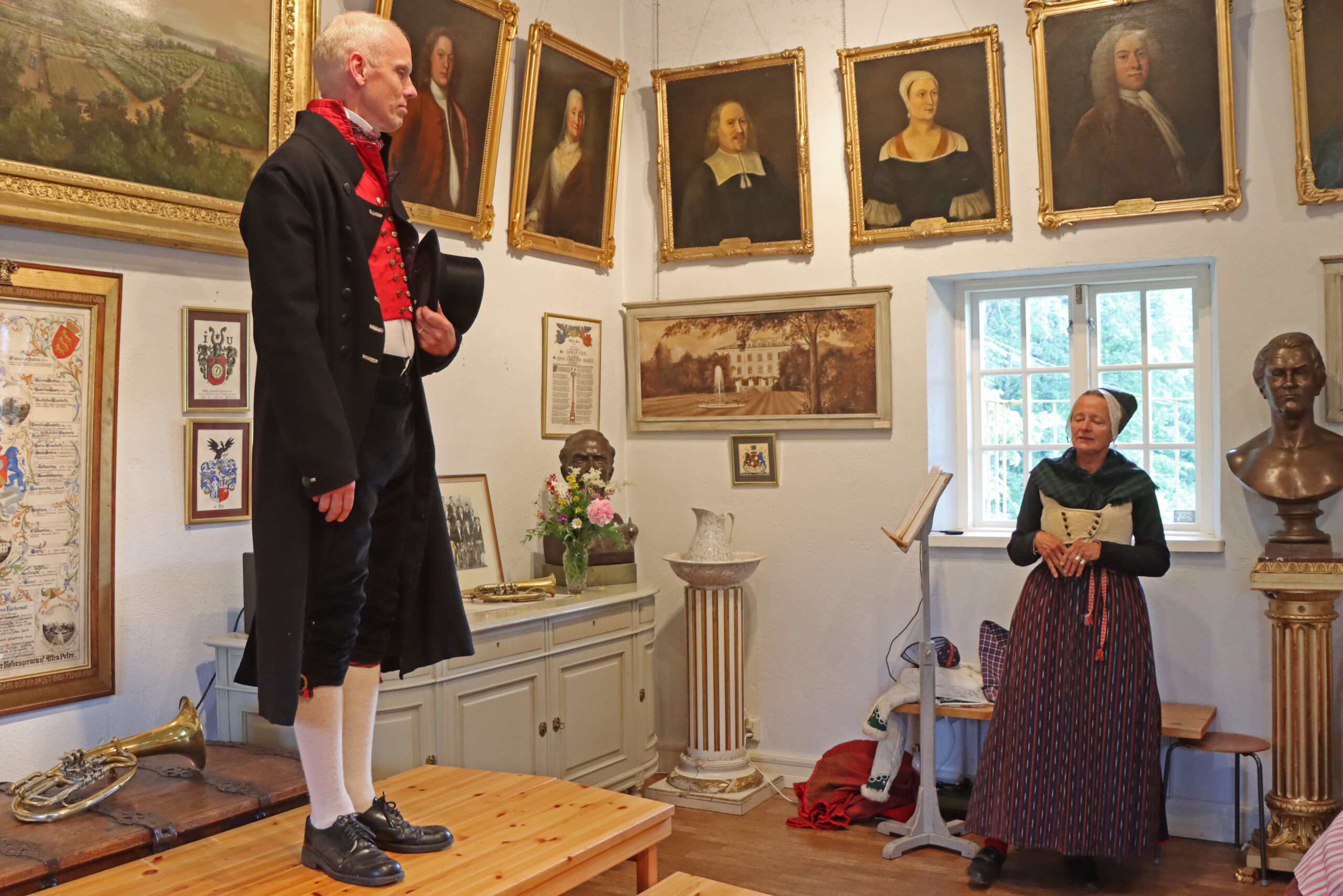 23_2183 Kyrkdräkt för man med svarta byxor, svart kyrkrock, hög hatt och väst i kattun. Vita strumpor. Modell Johannes Elnefred.