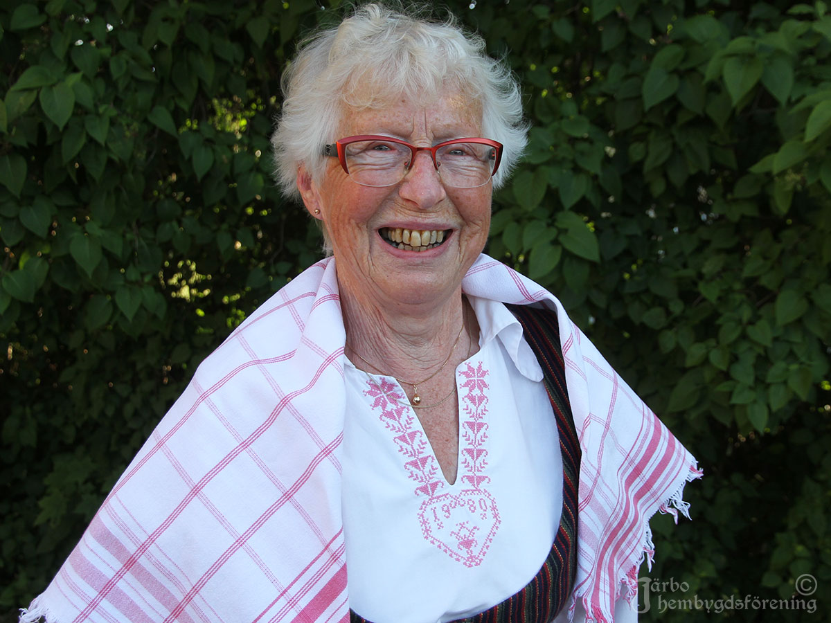 IMG_1863 Glad dam i sommarvariant av dräkt Ovansjö, Järbo. Randig livkjol och överdel i vitt med röda korsstygnsbroderier. Rödrutigt halskläde och kvistförkläde med röda och blå ränder.