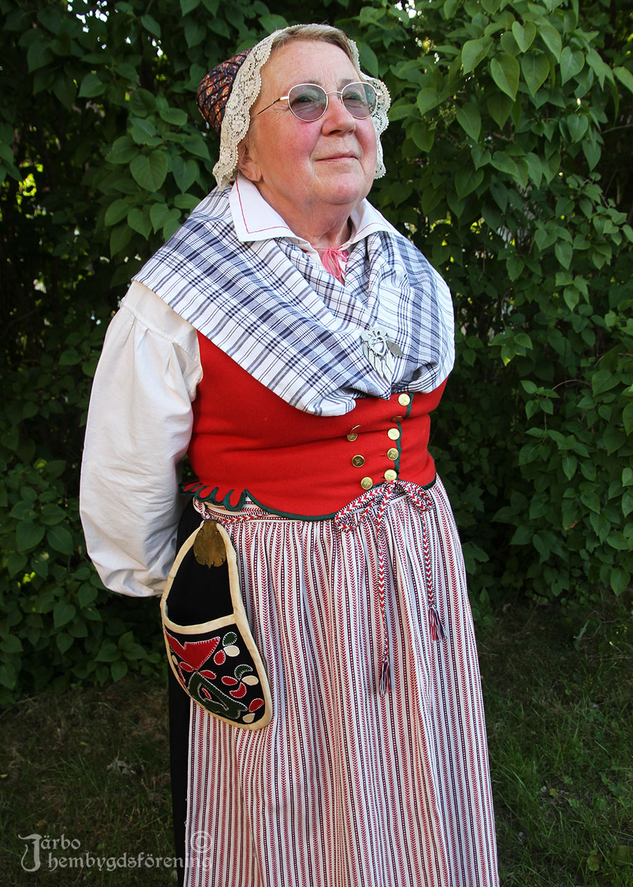 IMG_1895 Anna-Karin Modin njuter av solen i sin dräkt från Ovansjö med rött fläbblivstycke, svart kjol, rutigt halskläde och kvistförkläde.