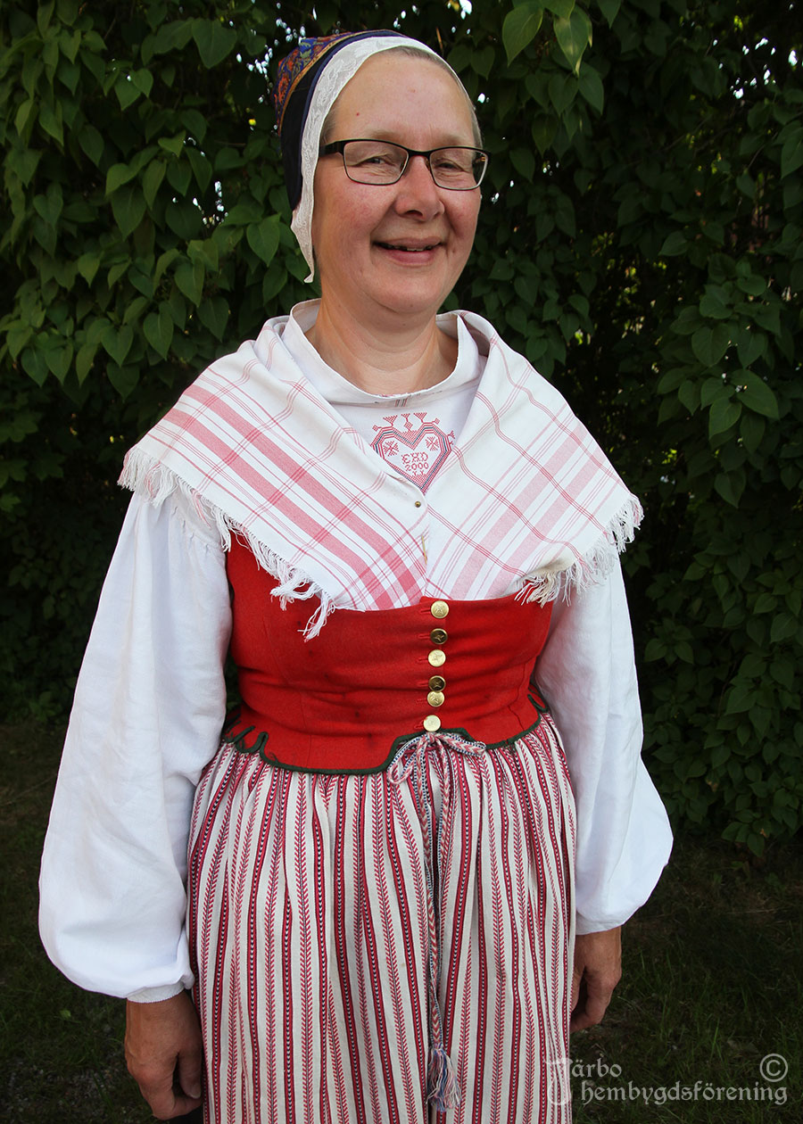 IMG_1932 Karin Skog har en variant av Ovansjödräkt med röda broderier på särken, rött halskläde, kvistförkläde i rött och likaså rött fläbblivstycke. Som huvudbonad skarpmössa med vitt stycke. Röda strumpor. Ogifta kvinnor brukade ha mera rött i sina dräkter, gifta brukade ha mera blått.