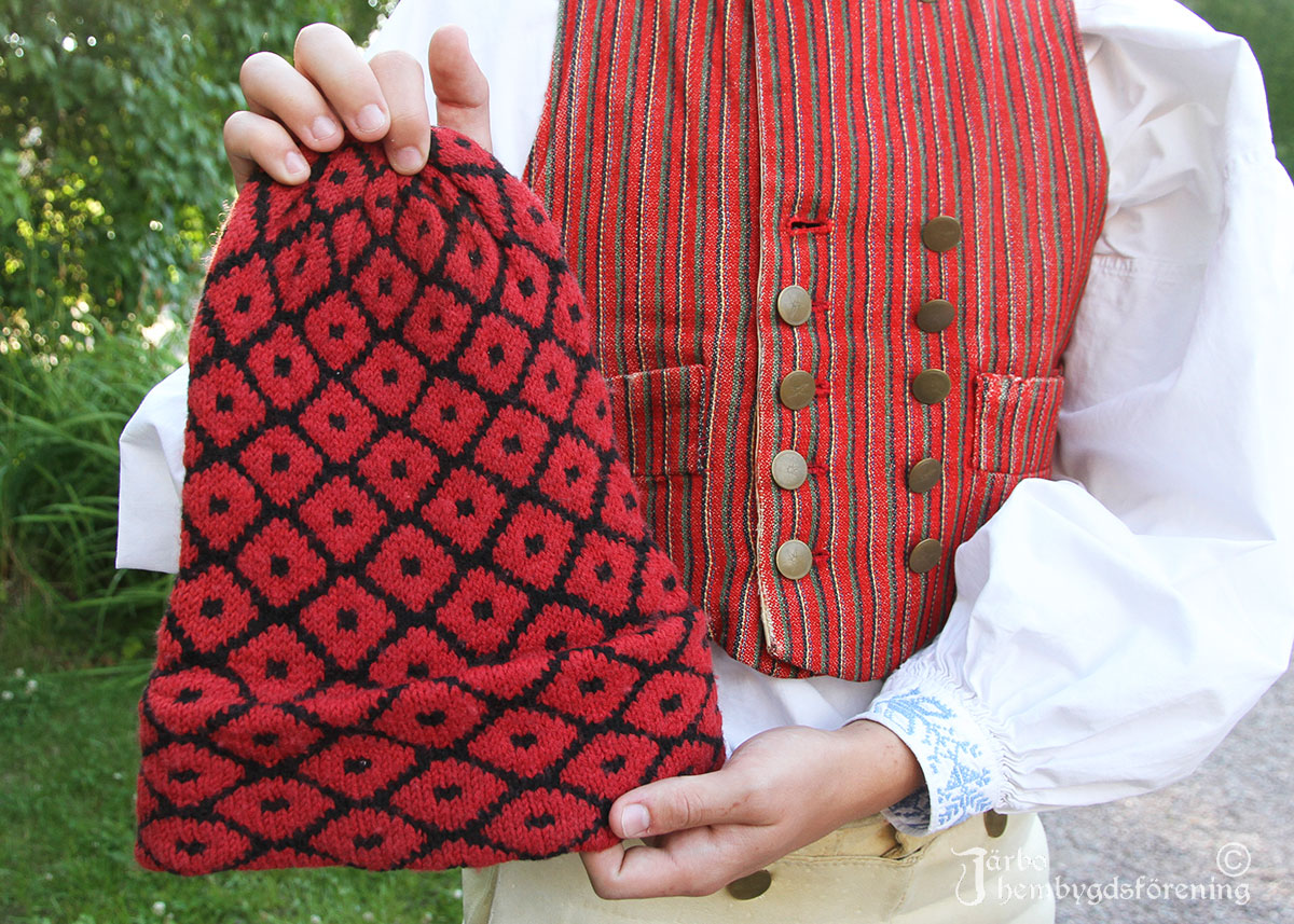 IMG_1939 Ulf visar upp den fina mönsterstickade mössan som ingick när hans farfar köpte en dräkt från Ovansjö för många år sen. Nu är det unge Ulf som klär sig i rödrandigt livstycke i kort empirmodell och gula knäbyxor. Väl använt och älskat, det syns på slitningarna i tyget.