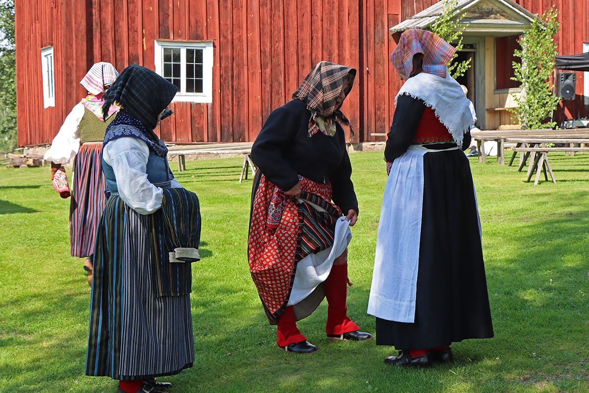 granslos_4175 En Ovansjökvinna från bild 3, Gunilla, möter kvinnnor från Svärdsjö på kyrkbacken och beundrar de fina röda snösockorna som används på vintern