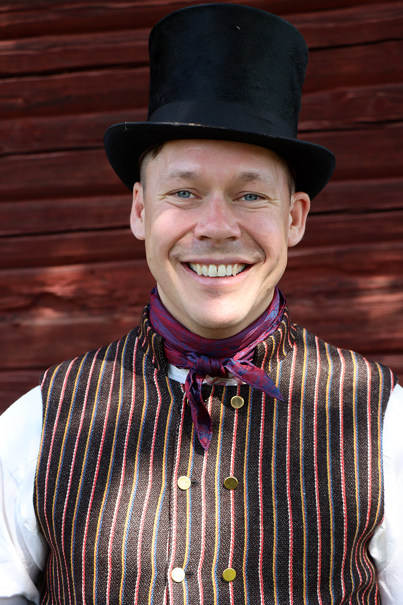 granslos_4197 Per är fin och klädd för allvarssöndag i hög svart hatt och mörkrandig väst med svarta byxor och blåa strumpor. Mörkt sidenhalskläde håller uppe kragen på den vita skjortan.