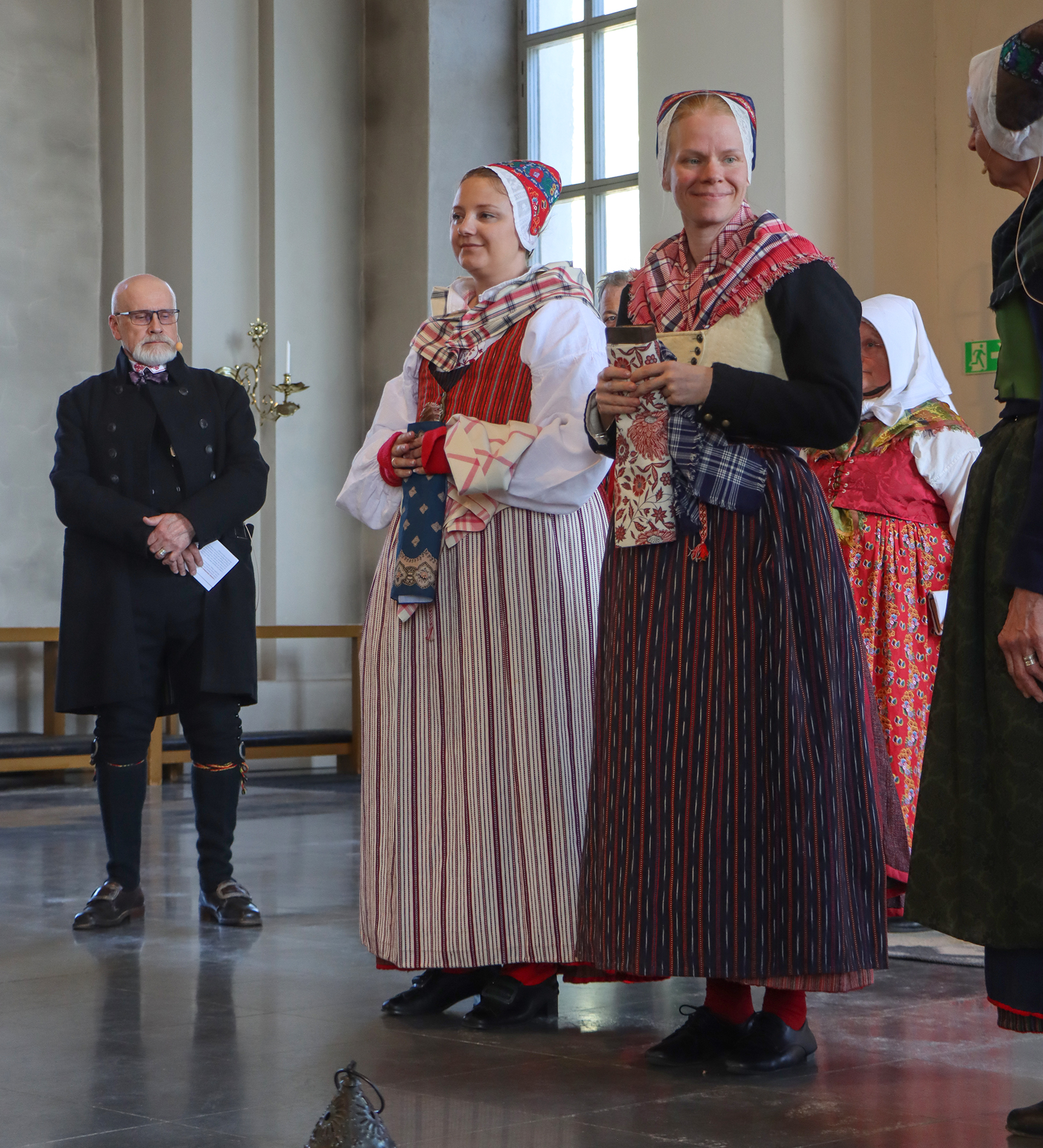 Modellerna gick in i grupper uppdelade efter klädsel under kyrkoåret. Emilia och Moa har enklare högtidsdräkt för helgfri sommar och vinter, ogift kvinna. Emilia har ett randigt fläbbliv, rött tvinnskört och ett rödrandigt förkläde med ljust rutigt halskläde och huvudkläde. Moa har livkjol med mörkare rött tvinnskört, svart tröja och skinnliv över samt förkläde och halskläde för vinter med rutigt huvudkläde