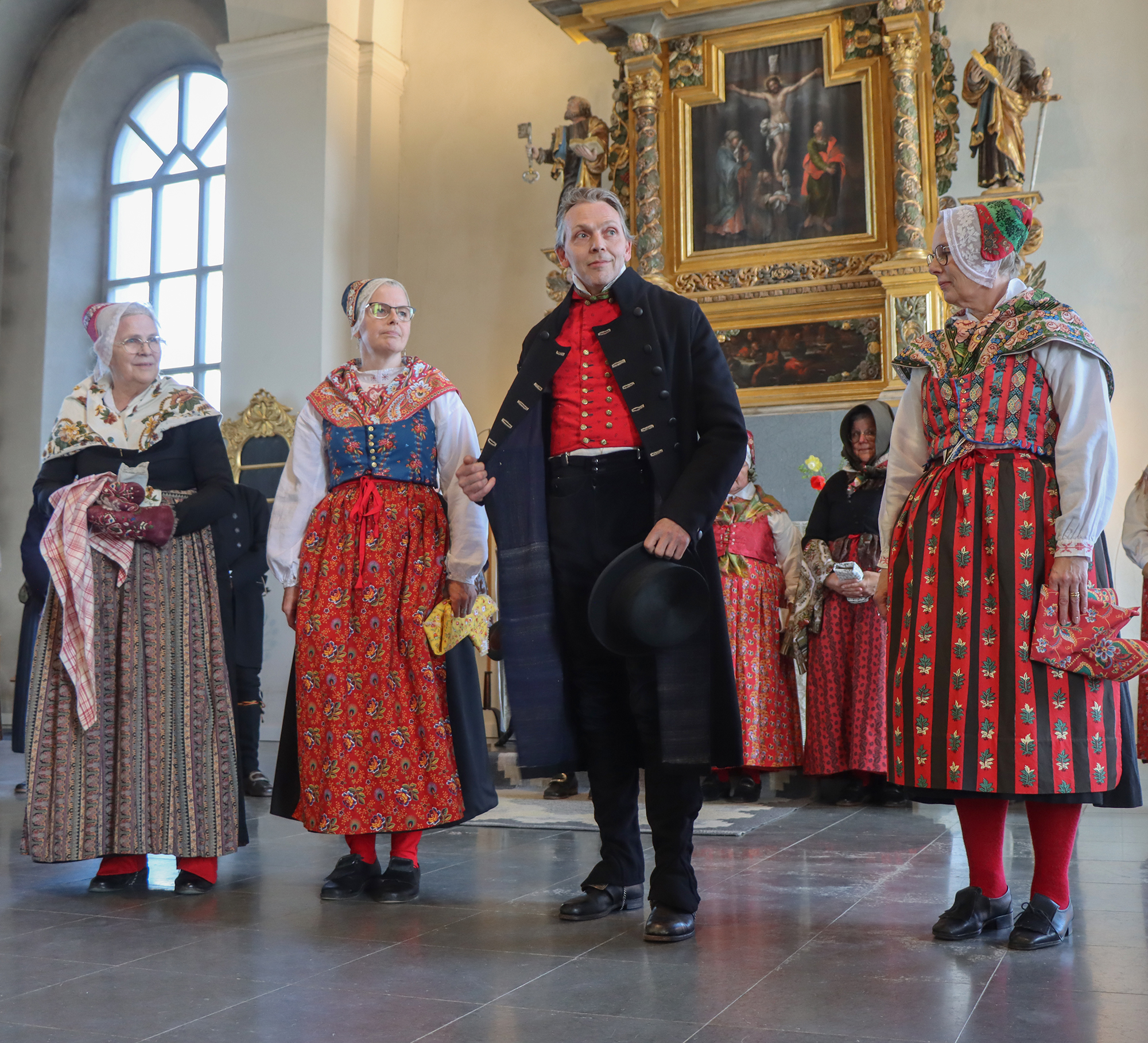 IMG_4818 Stilige Mikael bär kattunsväst, svarta byxor och långrock. Herrarna hade hög hatt till kyrkan och damerna hade huvudkläden i kattun. Tina har samma variant som Susanne, fast i andra färger. Dräkten kunde varieras inom vissa fastställda ramar, men det var viktigt att vara rätt klädd för rätt tillfälle i kyrkan.