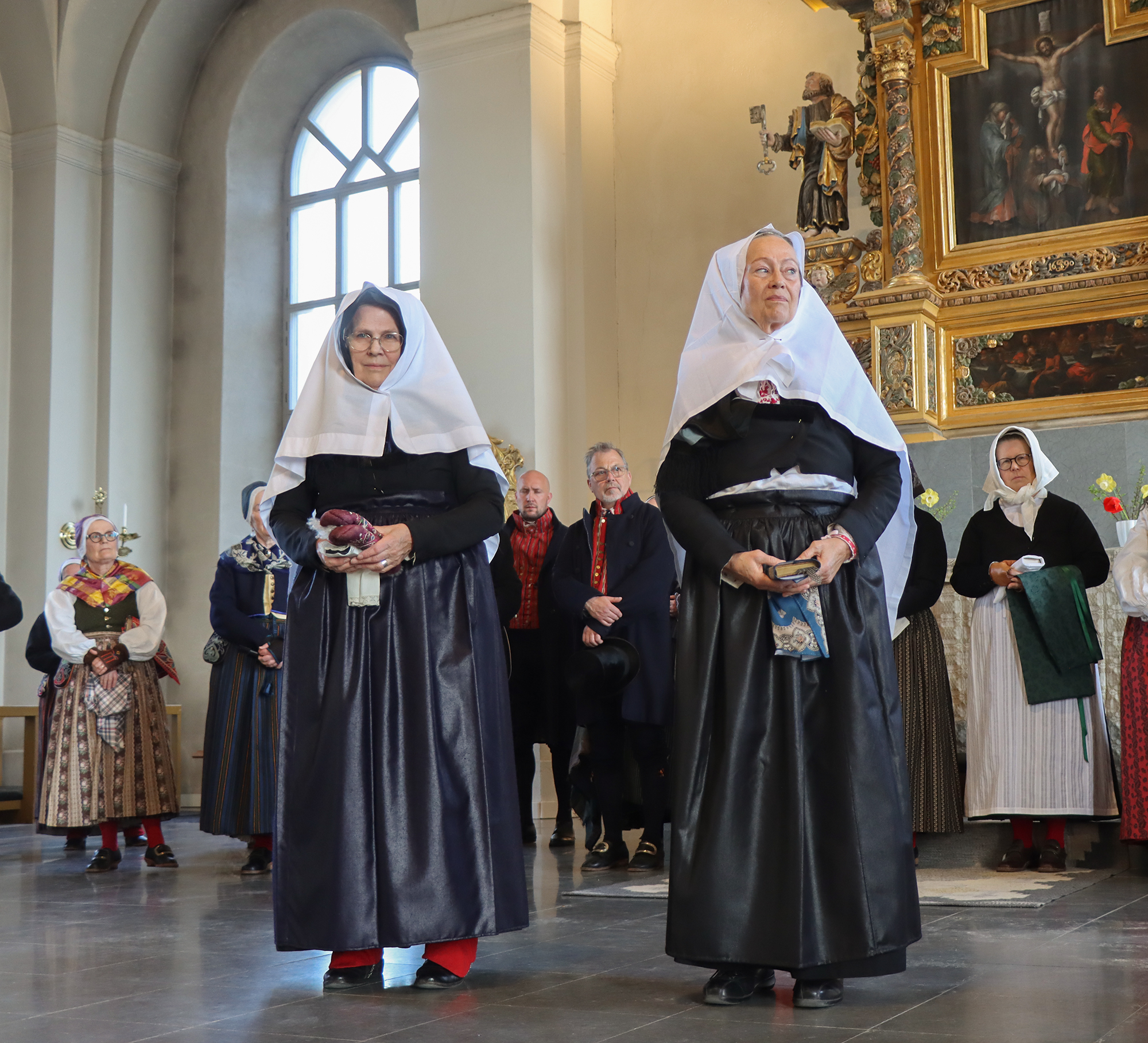 IMG_4849 Även sorg har sin speciella klädsel. Elisabeth och Gunilla bär båda ett stort vitt dok över sina svarta huvudkläden, svart tröja, svarta halskläden och svart kyrkkjol samt raskförkläden.